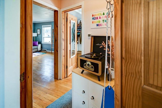 hall featuring light wood-style flooring, baseboards, and ornamental molding