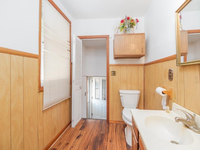 half bath featuring a wainscoted wall, wood finished floors, toilet, and wooden walls