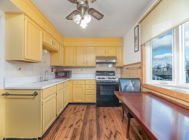 kitchen featuring under cabinet range hood, dark wood-style flooring, a sink, light countertops, and gas range oven