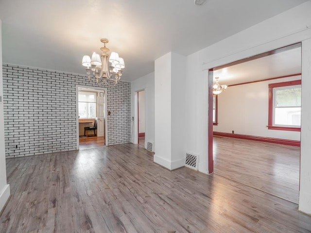 empty room with brick wall, visible vents, a notable chandelier, and wood finished floors