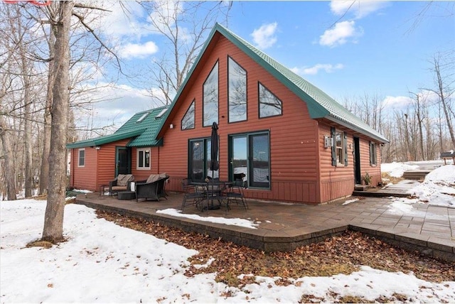 snow covered back of property featuring a patio and faux log siding