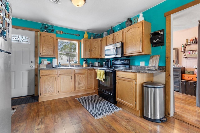 kitchen with black electric range, stainless steel microwave, a sink, and wood finished floors