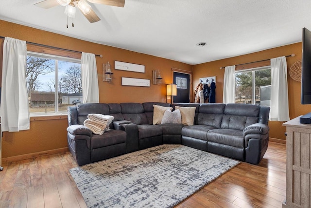 living area with ceiling fan, visible vents, light wood-style flooring, and baseboards