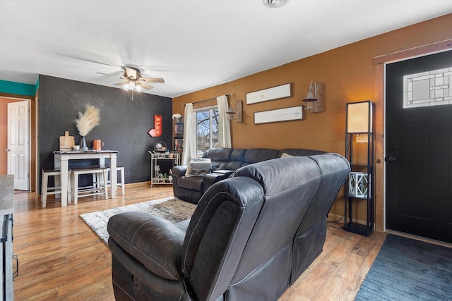 living area featuring a ceiling fan, light wood-type flooring, and baseboards