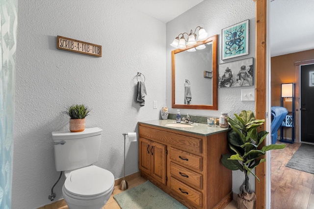 ensuite bathroom with toilet, vanity, connected bathroom, and a textured wall