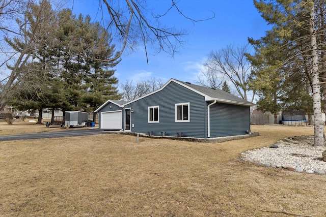 exterior space with aphalt driveway, a garage, fence, a yard, and a trampoline