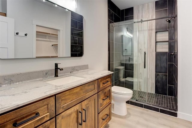 bathroom with toilet, a stall shower, wood finished floors, and vanity