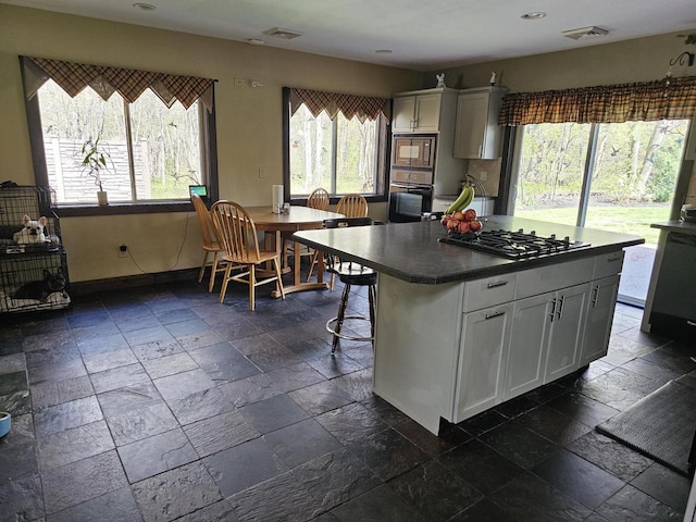 kitchen featuring stone tile floors, visible vents, white cabinets, built in microwave, and oven