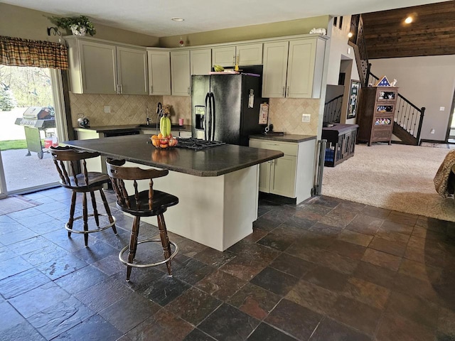 kitchen featuring stone tile floors, dark countertops, a kitchen breakfast bar, a center island, and black refrigerator with ice dispenser