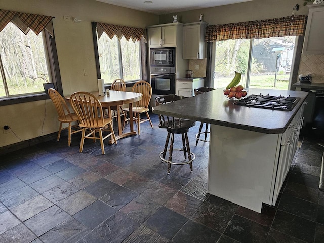 kitchen featuring stone tile floors, backsplash, a kitchen island, black appliances, and baseboards