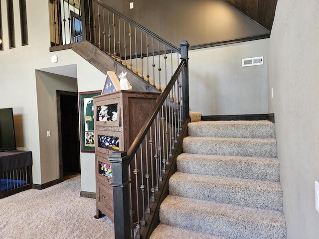 staircase featuring carpet floors, baseboards, a towering ceiling, and visible vents