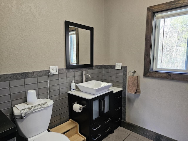 half bath with a healthy amount of sunlight, toilet, tile walls, and vanity