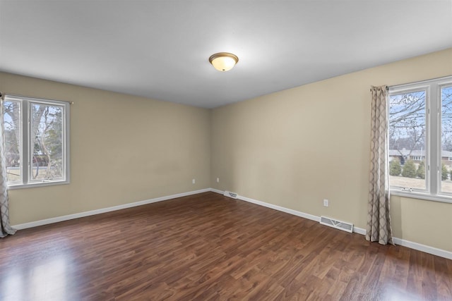 spare room featuring dark wood-style flooring, visible vents, and baseboards