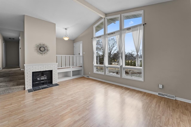 unfurnished living room with visible vents, a fireplace, lofted ceiling with beams, and wood finished floors