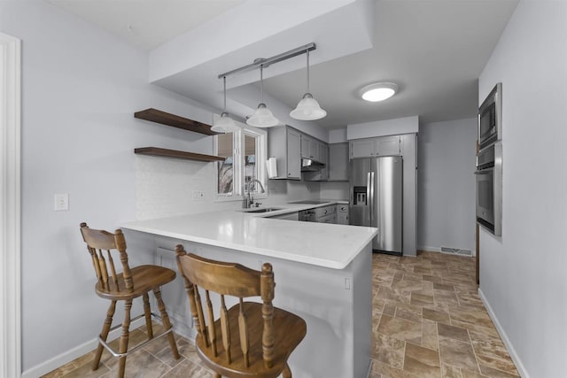 kitchen featuring gray cabinetry, stainless steel appliances, a peninsula, a sink, and stone finish floor