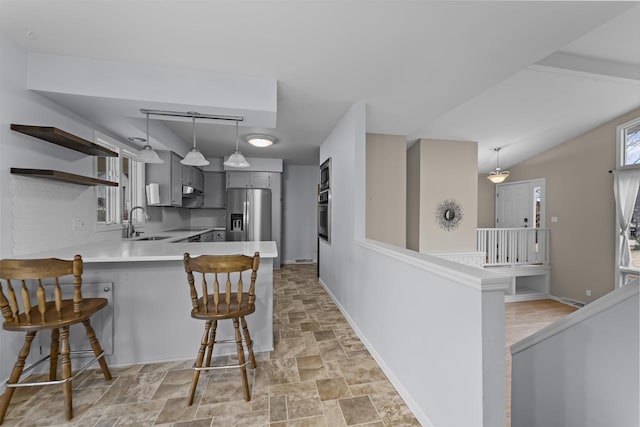 kitchen featuring a breakfast bar area, a peninsula, stainless steel appliances, gray cabinetry, and a sink