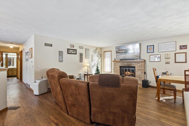 living area with dark wood-style floors, baseboards, a brick fireplace, and visible vents