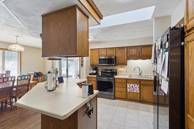 kitchen with decorative light fixtures, stainless steel appliances, light countertops, brown cabinetry, and a sink