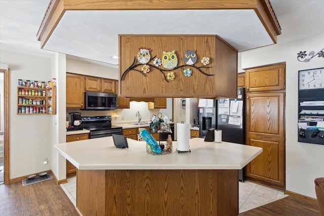 kitchen with brown cabinetry, stainless steel microwave, black range with electric stovetop, light countertops, and a sink