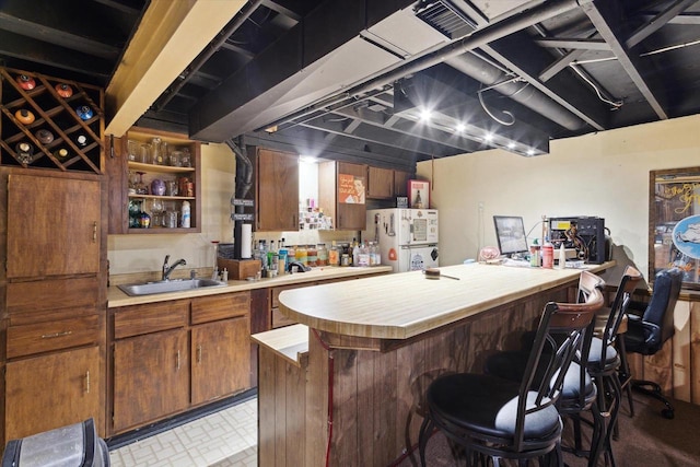 interior space with brown cabinetry, a kitchen breakfast bar, freestanding refrigerator, a peninsula, and a sink