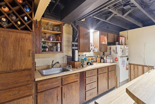 kitchen featuring open shelves, light countertops, brown cabinetry, freestanding refrigerator, and a sink