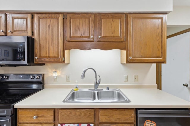 kitchen featuring stainless steel appliances, brown cabinetry, a sink, and light countertops