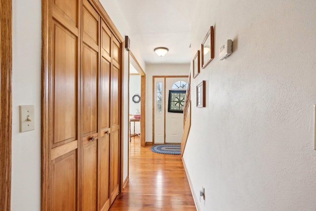 corridor featuring light wood finished floors and baseboards