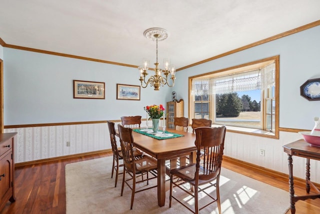 dining space featuring a chandelier, a wainscoted wall, wood finished floors, baseboards, and ornamental molding