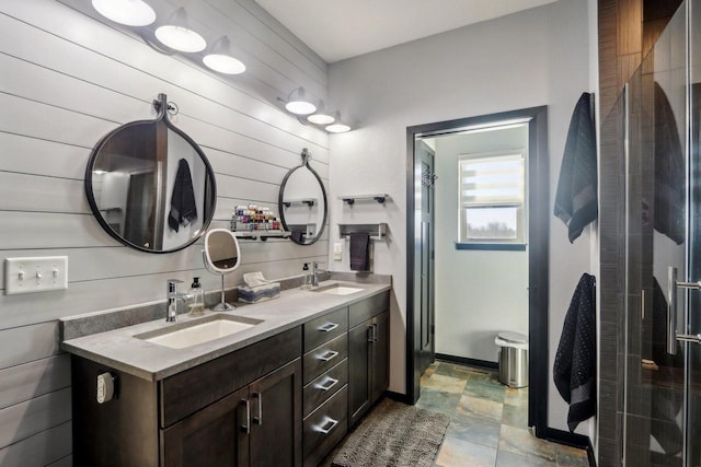 bathroom featuring double vanity, wood walls, a shower stall, and a sink