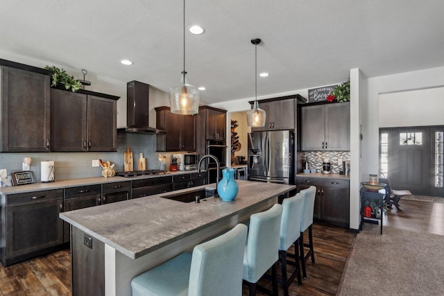 kitchen with dark wood finished floors, stainless steel appliances, a sink, wall chimney range hood, and dark brown cabinetry