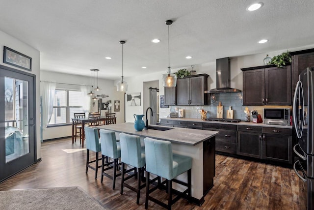 kitchen with tasteful backsplash, dark wood finished floors, wall chimney exhaust hood, appliances with stainless steel finishes, and a sink