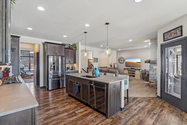 kitchen with stainless steel appliances, light countertops, open floor plan, a sink, and dark brown cabinets