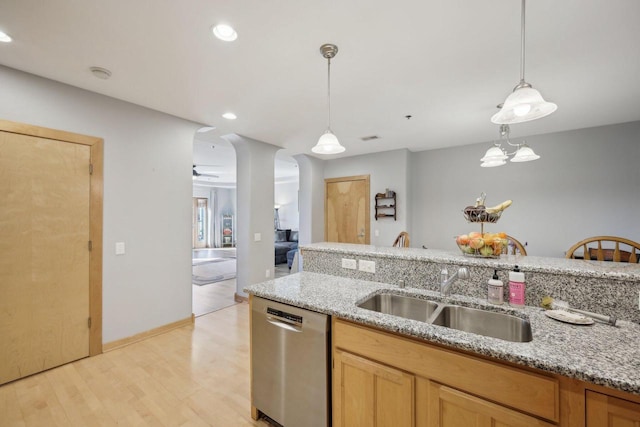 kitchen with a sink, light wood-style flooring, light stone counters, and dishwasher