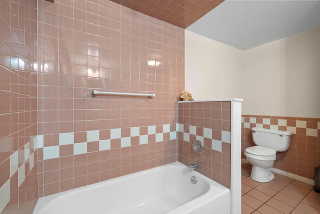 full bath featuring a washtub, toilet, a wainscoted wall, tile walls, and tile patterned floors