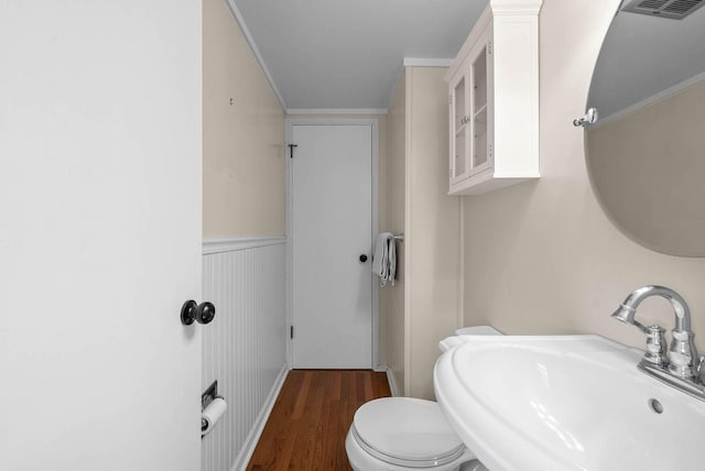 half bathroom with toilet, wood finished floors, visible vents, a sink, and wainscoting