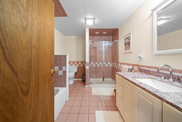 bathroom featuring a stall shower, wainscoting, toilet, tile patterned floors, and tile walls