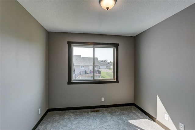 carpeted empty room with a textured ceiling, visible vents, and baseboards