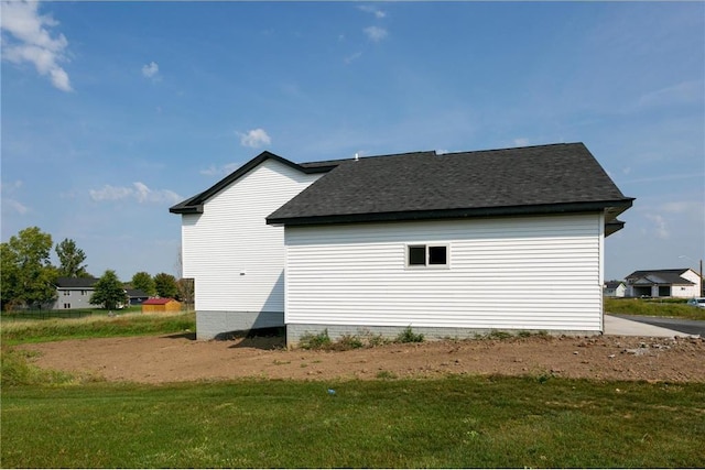 view of side of property featuring a shingled roof and a yard