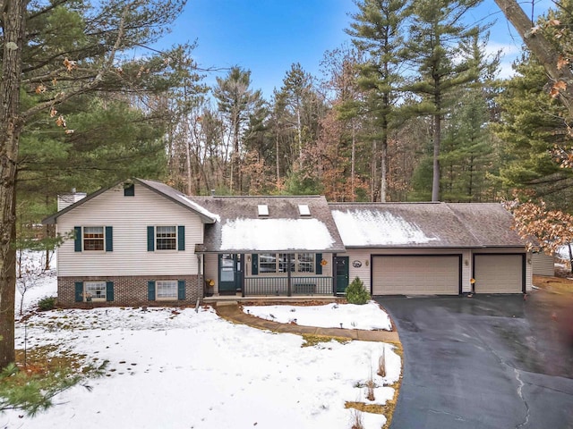 split level home featuring a garage, aphalt driveway, covered porch, and brick siding