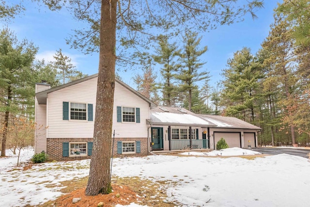 tri-level home featuring a garage, aphalt driveway, a chimney, and brick siding