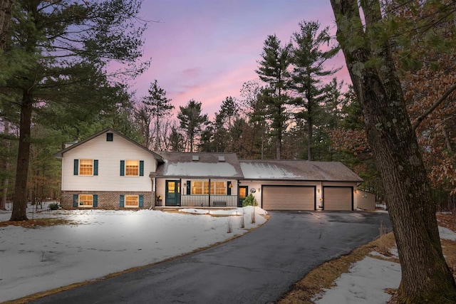 split level home with a garage, covered porch, brick siding, and driveway