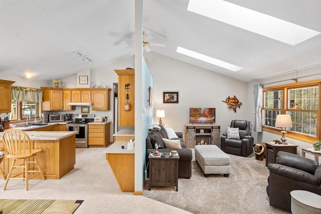 living area featuring light tile patterned floors, vaulted ceiling with skylight, a ceiling fan, a lit fireplace, and track lighting