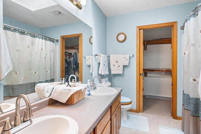 bathroom with double vanity, a walk in closet, a sink, and tile patterned floors