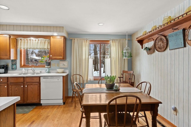 kitchen with brown cabinetry, dishwasher, light countertops, light wood-style floors, and a sink