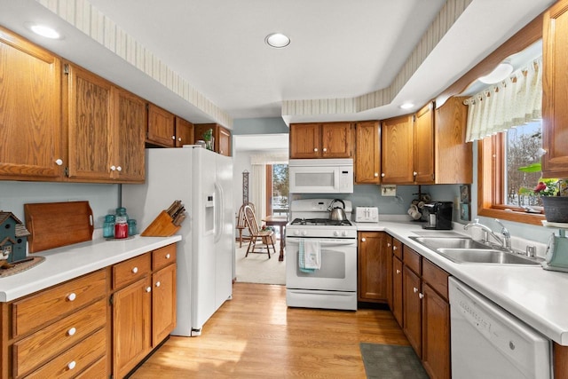 kitchen with light countertops, white appliances, a sink, and light wood-style flooring