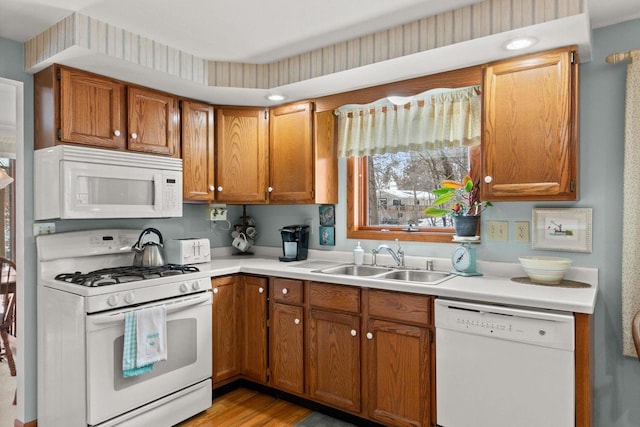 kitchen with light countertops, white appliances, brown cabinetry, and a sink