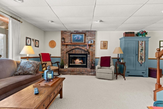 living room featuring a brick fireplace, carpet, and a drop ceiling