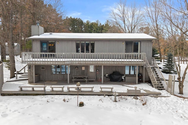 snow covered rear of property featuring a deck, stairway, and a chimney