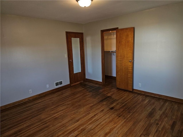 unfurnished bedroom with a closet, visible vents, dark wood finished floors, and baseboards