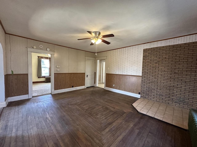 spare room featuring ornamental molding, wainscoting, dark wood finished floors, and a ceiling fan